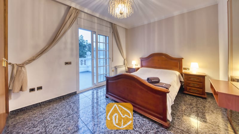 Vakantievilla's Costa Brava Spanje - Villa Rosa - Slaapkamer voorzien van een houten bedframe, tegelvloer en glazen schuifdeuren die toegang bieden tot een buitenbalkon.
