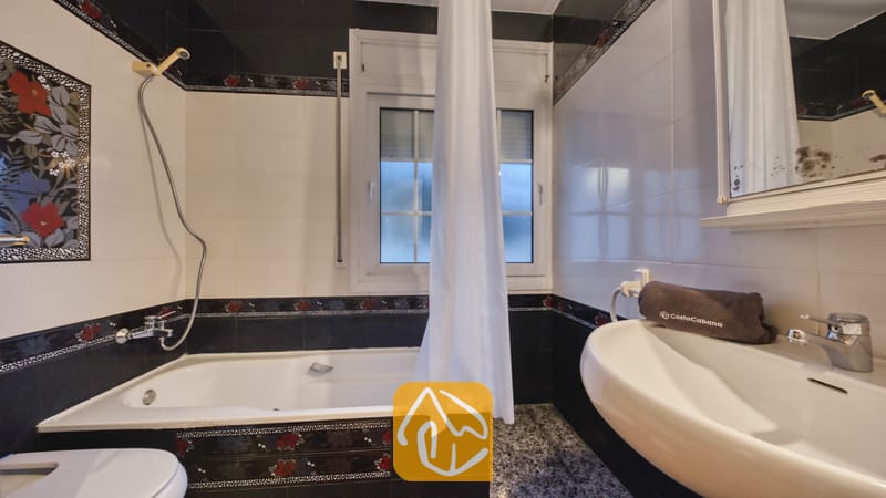 Vakantievilla's Costa Brava Spanje - Villa Rosa - Badkamer met een wit ligbad, aangesloten douchekop en zwart-wit betegelde muren, gedecoreerd met rode bloemmotieven.
