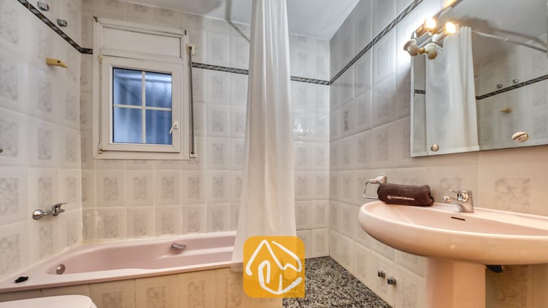 Vakantievilla's Costa Brava Spanje - Villa Rosa - Badkamer met een lichtroze ligbad, bijpassende wastafel op zuil, witte wandtegels met een decoratieve rand en een klein raam met melkglas.