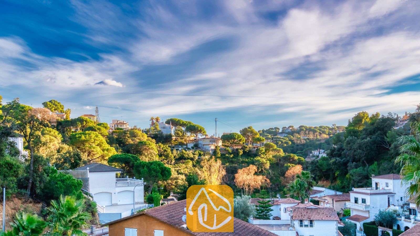 Vakantievilla's Costa Brava Spanje - Villa Rosa - Verheven uitzicht vanuit Villa Rosa over een Spaanse heuvelwijk met witte huizen, terracotta daken en groene bomen onder een blauwe hemel met slierten witte wolken