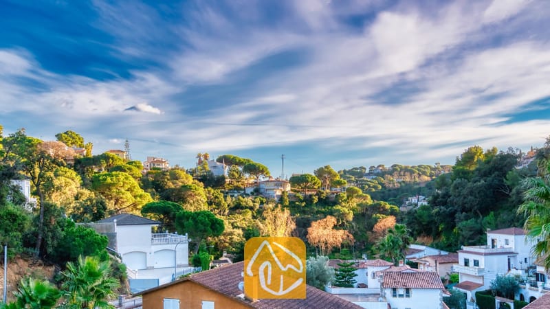 Vakantievilla's Costa Brava Spanje - Villa Rosa - Verheven uitzicht vanuit Villa Rosa over een Spaanse heuvelwijk met witte huizen, terracotta daken en groene bomen onder een blauwe hemel met slierten witte wolken