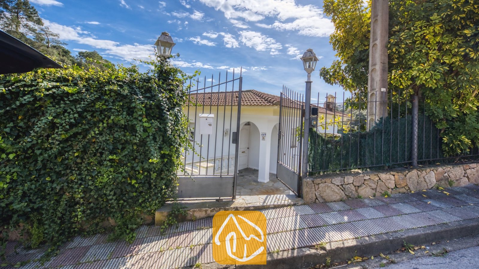 Vakantievilla's Costa Brava Spanje - Villa Rosa - Toegangspoort van Villa Rosa met een metalen hek, een met klimop begroeide stenen muur en uitzicht op de witte buitenkant met pannendak.