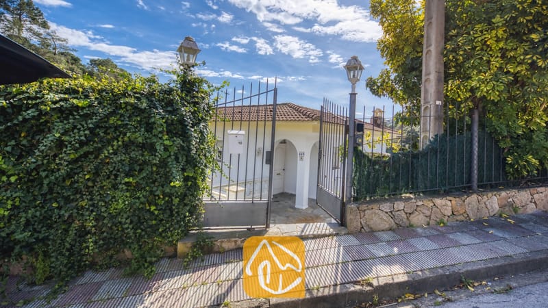 Vakantievilla's Costa Brava Spanje - Villa Rosa - Toegangspoort van Villa Rosa met een metalen hek, een met klimop begroeide stenen muur en uitzicht op de witte buitenkant met pannendak.