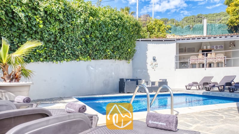 Vakantievilla's Costa Brava Spanje - Villa Rosa - Privézwembad bij Villa Rosa met donkere ligbedden en opgevouwen handdoeken, een terras met zitje en een hoge keermuur bedekt met weelderige, groene klimop.
