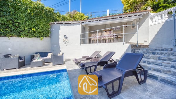 Vakantievilla's Costa Brava Spanje - Villa Rosa - Het privézwembadgedeelte van Villa Rosa, voorzien van donkergrijze kunststof ligbedden op een betegeld terras, een buitenloodsset met kussens en een overdekt terras erboven.