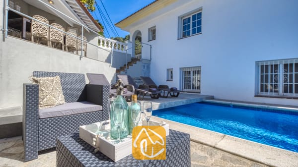 Vakantievilla's Costa Brava Spanje - Villa Rosa - Privézwembad bij Villa Rosa met grijs vlechtwerk tuingemeubilair, een wit houten serveerblad met glaswerk en ligstoelen op het terras.