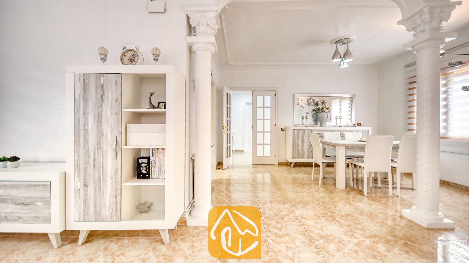Vakantievilla's Costa Brava Spanje - Villa Sarai - Witte eethoek en woonkamer in Villa Sarai, voorzien van tegelvloeren, decoratieve zuilen en wittemeesubels met houten accenten.
