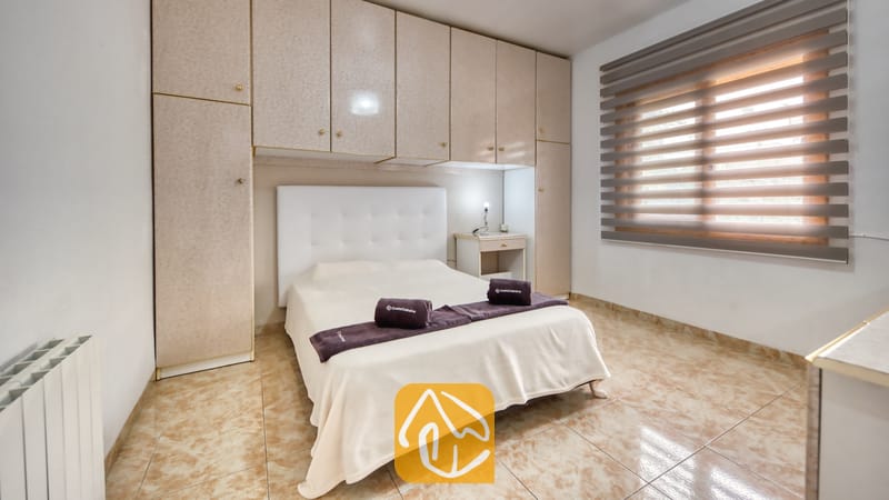 Vakantievilla's Costa Brava Spanje - Villa Sarai - Slaapkamer voorzien van een wit gestoffeerd hoofdeinde, ingebouwde beige kasten en een raam met horizontale jaloezieën.