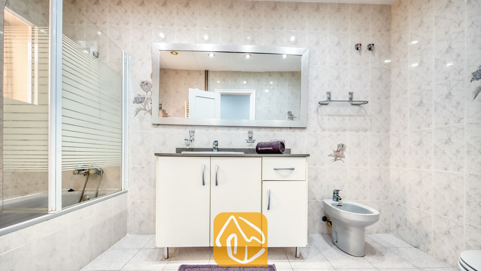 Vakantievilla's Costa Brava Spanje - Villa Sarai - Badkamer voorzien van een wit badkamermeubel met een donker aanrechtblad, een grote spiegel, een bidet en een ligbad met glazen wand.