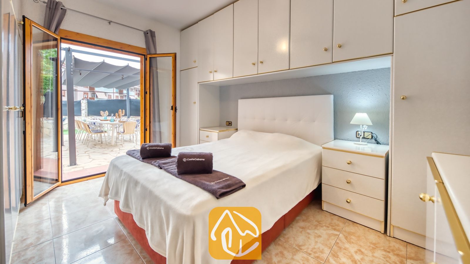 Vakantievilla's Costa Brava Spanje - Villa Sarai - Slaapkamer met een tweepersoonsbed, witte inbouwkasten, bijpassende nachtkastjes en open glazen deuren die leiden naar een buitenterras.