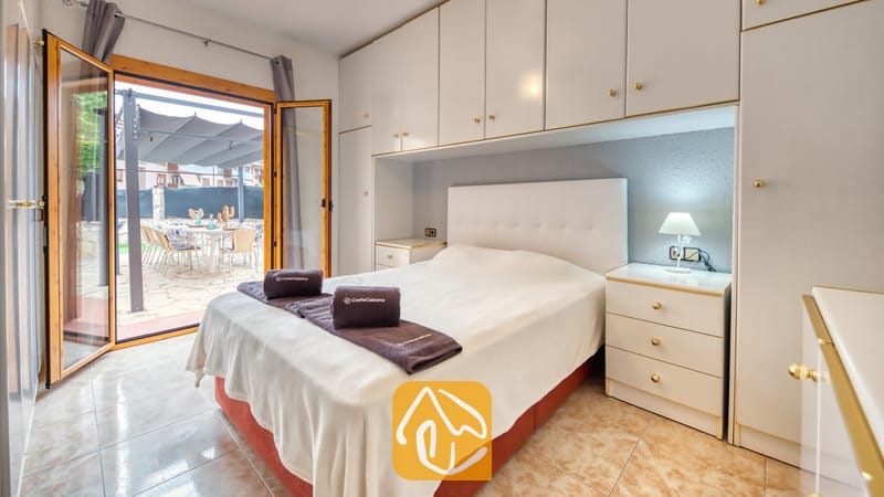 Vakantievilla's Costa Brava Spanje - Villa Sarai - Slaapkamer met een tweepersoonsbed, witte inbouwkasten, bijpassende nachtkastjes en open glazen deuren die leiden naar een buitenterras.