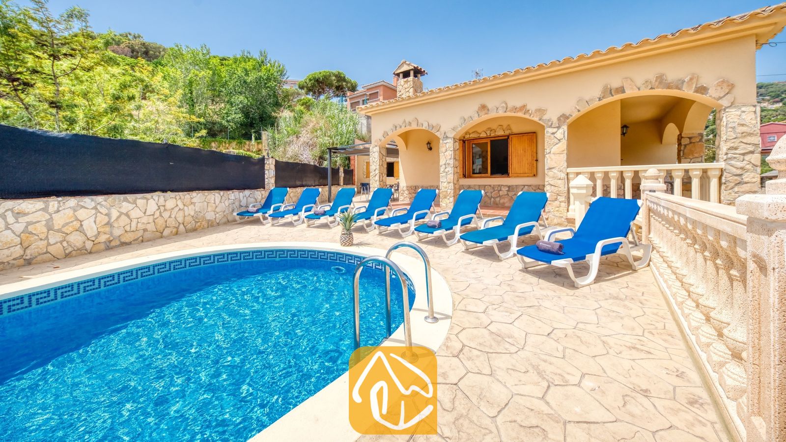Vakantievilla's Costa Brava Spanje - Villa Sarai - Gebogen buitenzwembad met blauw water en metalen handgrepen bij Villa Sarai, omringd door blauwe ligstoelen en een stenen terras.