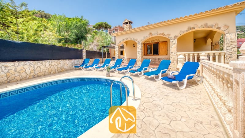 Vakantievilla's Costa Brava Spanje - Villa Sarai - Gebogen buitenzwembad met blauw water en metalen handgrepen bij Villa Sarai, omringd door blauwe ligstoelen en een stenen terras.