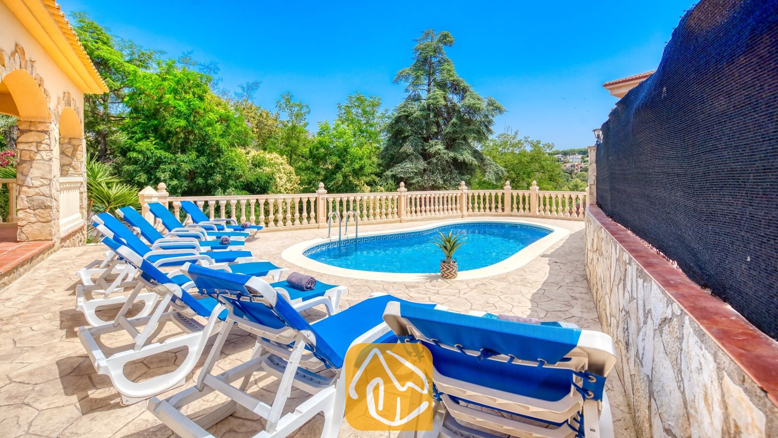 Vakantievilla's Costa Brava Spanje - Villa Sarai - Privé buitenzwembad bij Villa Sarai, omringd door blauwe ligstoelen, stenen terrastegels en groene bomen onder een heldere, blauwe hemel