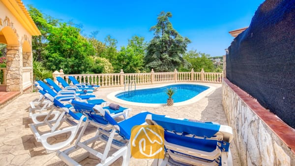 Vakantievilla's Costa Brava Spanje - Villa Sarai - Privé buitenzwembad bij Villa Sarai, omringd door blauwe ligstoelen, stenen terrastegels en groene bomen onder een heldere, blauwe hemel