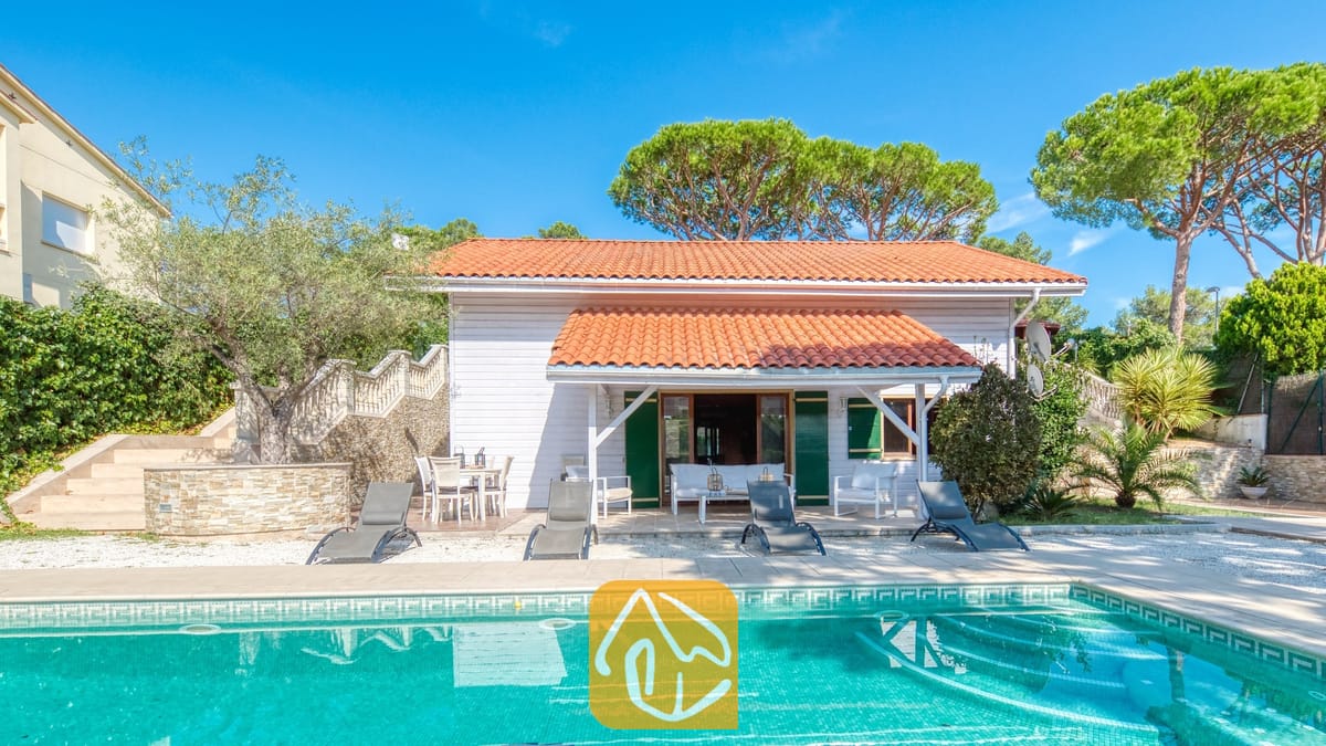 Vakantievilla's Costa Brava Spanje - Villa PrimaDonna - Buitenaanzicht van Villa PrimaDonna met een eigen zwembad met turkoois water, vier donkere ligbedden en een witte houten villa met een oranje pannendak.
