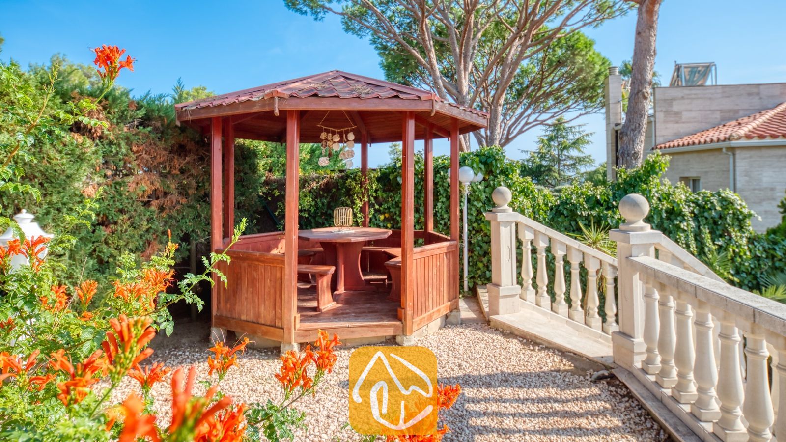 Vakantievilla's Costa Brava Spanje - Villa PrimaDonna - Houten priëel met een tafel en ingebouwde banken in de tuin van Villa PrimaDonna, naast een stenen balustrade trap.