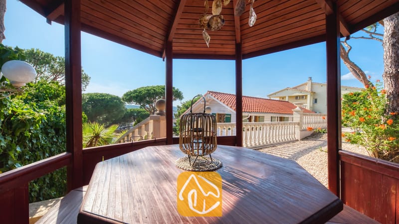 Vakantievilla's Costa Brava Spanje - Villa PrimaDonna - Houten prieel met een zeshoekige tafel en rieten lantaarn, uitkijkend over een tuinterras met terracotta dakpannen bij Villa PrimaDonna.