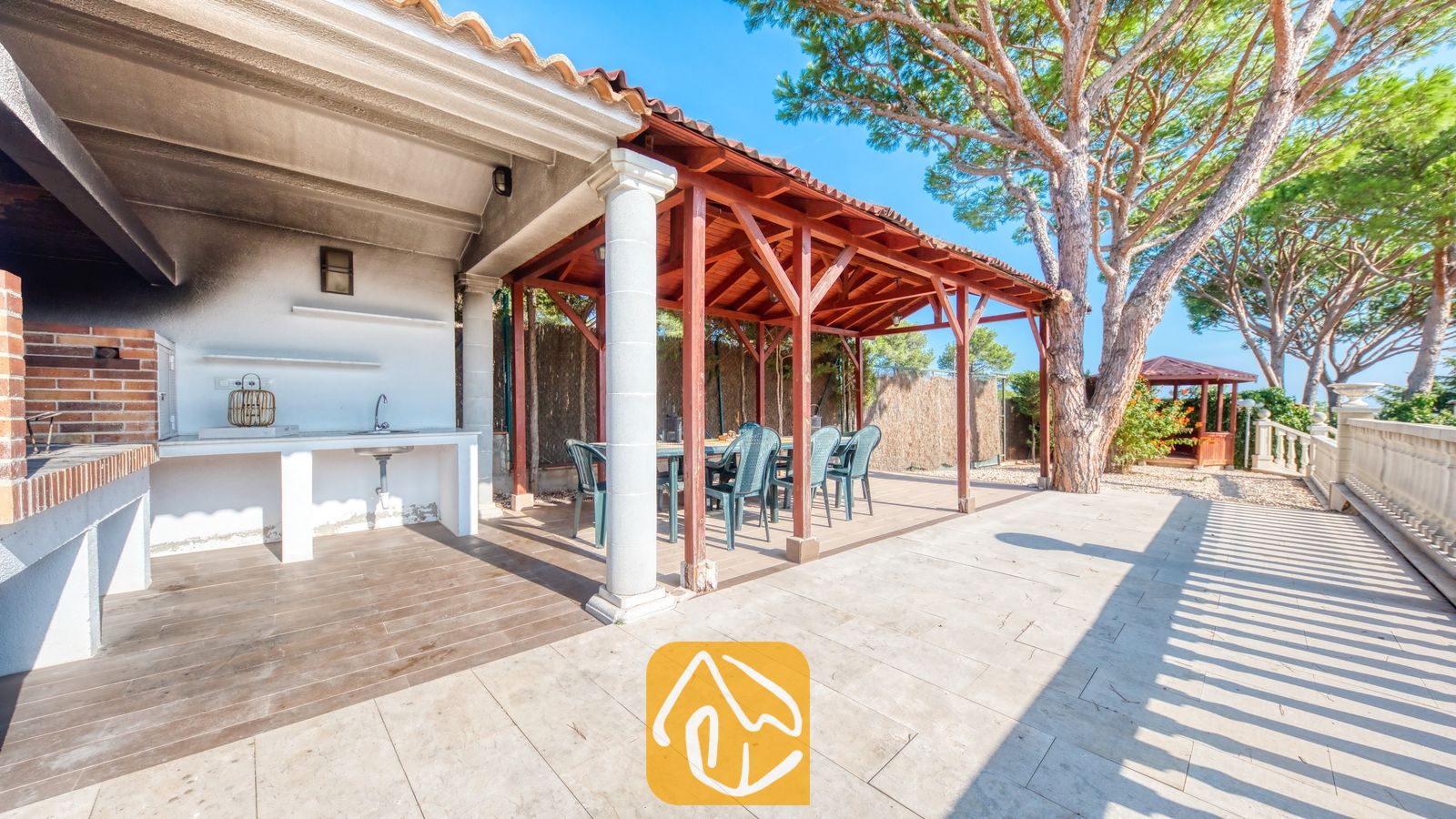 Vakantievilla's Costa Brava Spanje - Villa PrimaDonna - Buiteniterras van Villa PrimaDonna met een overdekte eethoek met houten balken, een stenen barbecue-aanrecht met wasbak en omringd door dennenbomen.