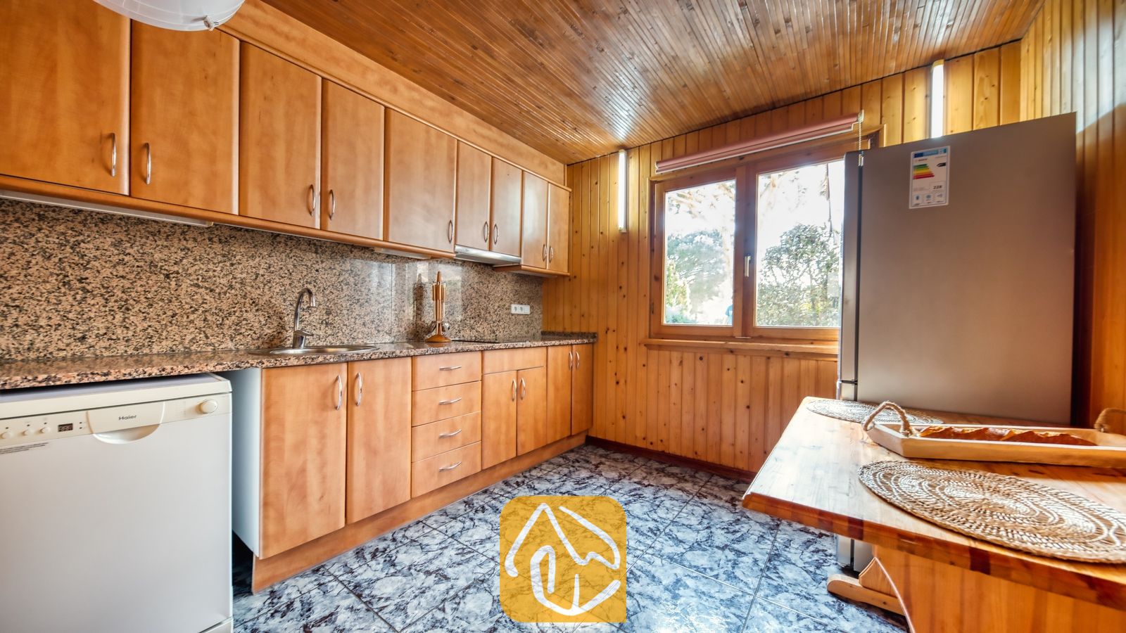 Vakantievilla's Costa Brava Spanje - Villa PrimaDonna - Keuken met houten kasten, muren en plafonds met houten panelen, granieten aanrechtbladen en een tegelvloer, voorzien van een ingebouwde gootsteen, vaatwasser en koelkast.
