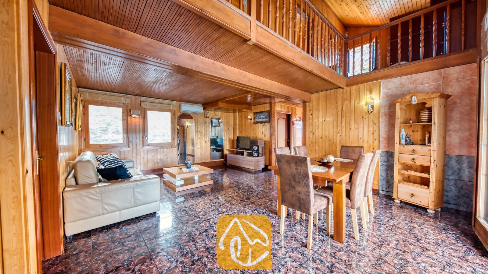 Vakantievilla's Costa Brava Spanje - Villa PrimaDonna - Ruime, houten woon- en eetkamer in Villa PrimaDonna, voorzien van een crèmelederen bank, een houten eettafel met bruine stoelen en een open vide erboven.