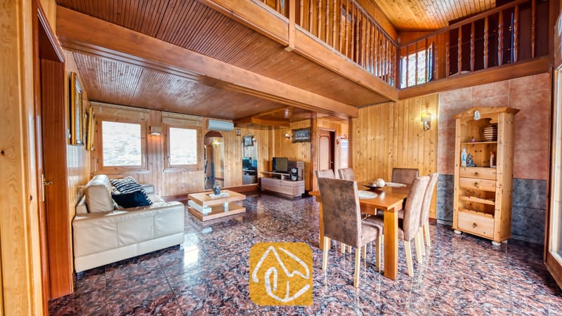 Vakantievilla's Costa Brava Spanje - Villa PrimaDonna - Ruime, houten woon- en eetkamer in Villa PrimaDonna, voorzien van een crèmelederen bank, een houten eettafel met bruine stoelen en een open vide erboven.