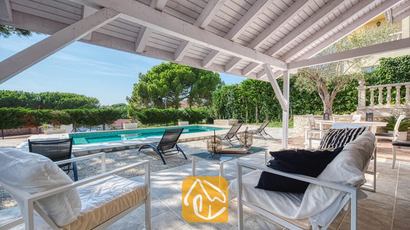 Vakantievilla's Costa Brava Spanje - Villa PrimaDonna - Overdekt buitenpatio bij Villa PrimaDonna met witte houten balken, tegelvloer, zitmeubilair en een buitenzwembad op de achtergrond.