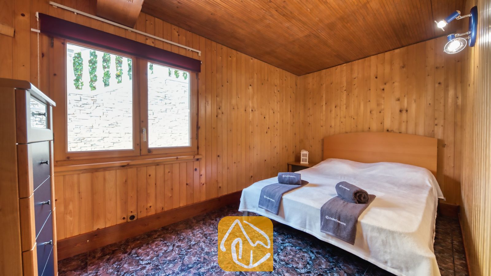 Vakantievilla's Costa Brava Spanje - Villa PrimaDonna - Slaapkamer met houten lambrisering op de muren en het plafond, een tweepersoonsbed met grijs opgevouwen handdoeken en een tegelvloer met patroon.