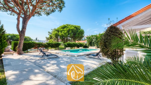 Vakantievilla's Costa Brava Spanje - Villa PrimaDonna - Buitenzwembad bij Villa PrimaDonna met een grindterras, zwarte ligbedden en volwassen dennenbomen onder een blauwe hemel