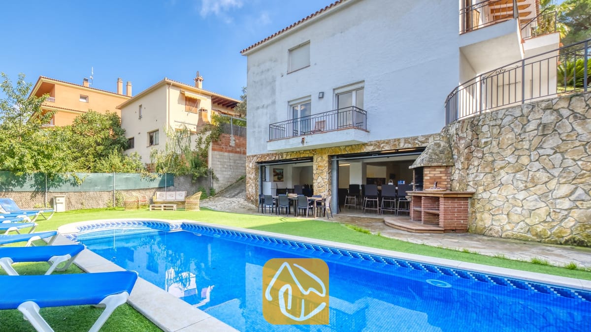 Vakantievilla's Costa Brava Spanje - Villa Nicky - Privézwembad met blauwe ligstoelen en een stenen terras bij Villa Nicky, met een witte, meerdere verdiepingen tellende buitenzijde, een buitenbarbecue en een open eetterras.