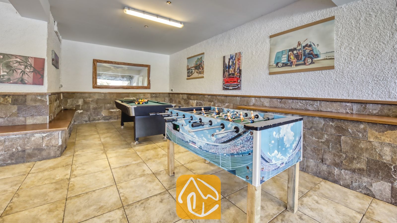 Vakantievilla's Costa Brava Spanje - Villa Nicky - Spelkamer bij Villa Nicky met op de voorgrond een tafelvoetbalspel met stadiongraphics, een biljarttafel op de achtergrond, natuurstenen muren en ingelijste kunstwerken.