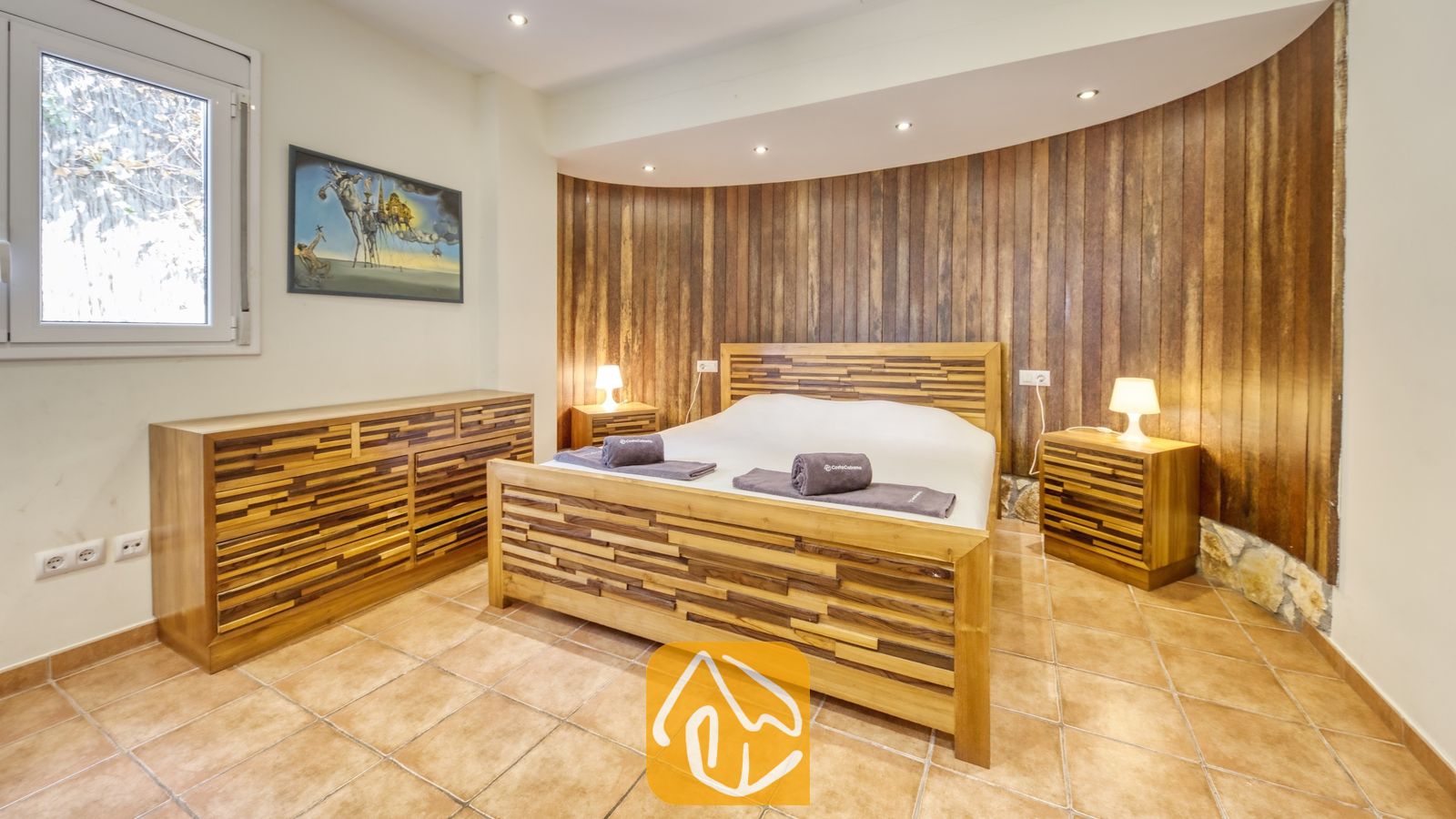Vakantievilla's Costa Brava Spanje - Villa Nicky - Slaapkamer met een houten bedframe, bijpassende nachtkastjes met lampen en een gebogen houten lattenwand als accentmuur achter het bed.