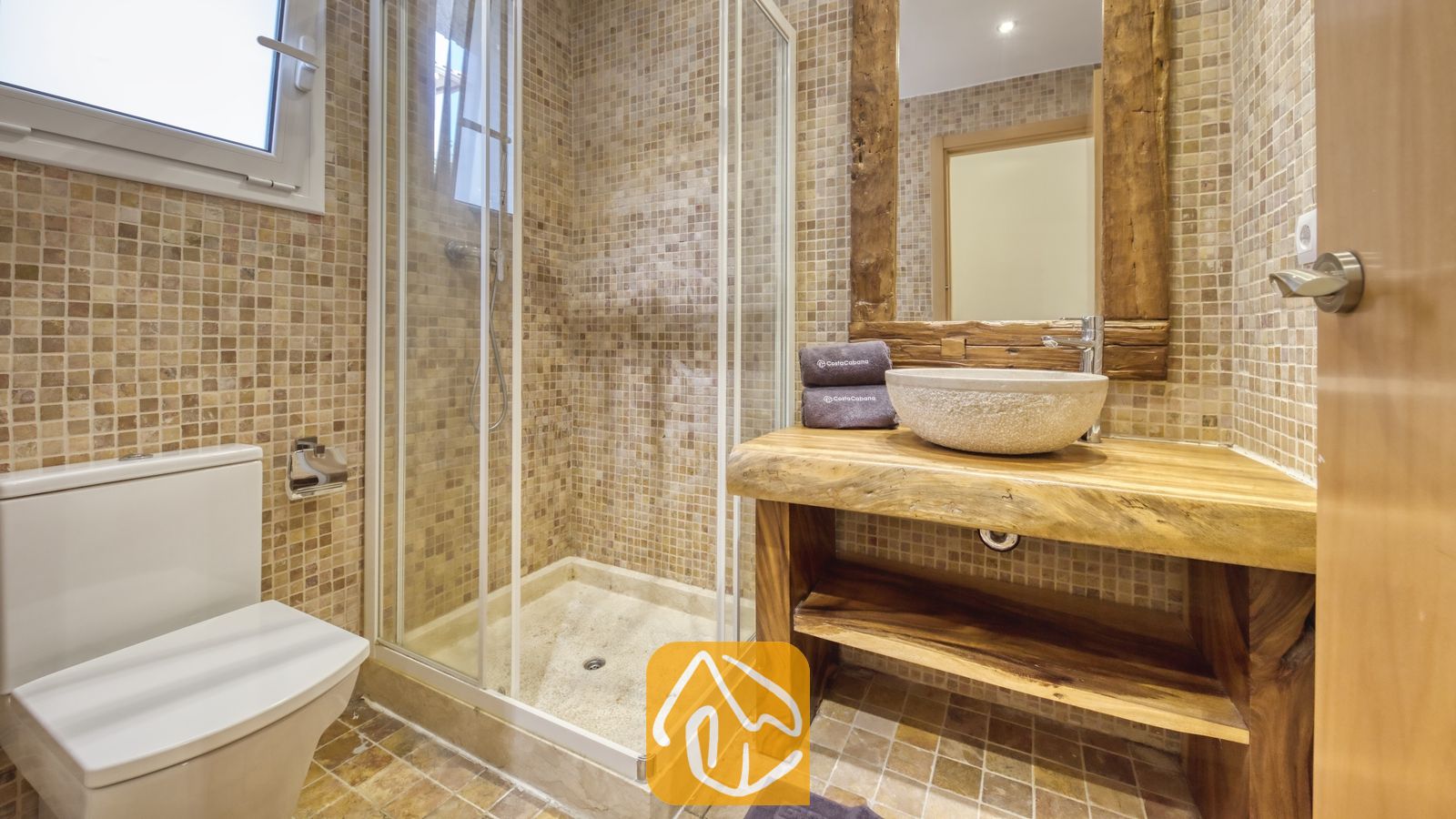 Vakantievilla's Costa Brava Spanje - Villa Nicky - Badkamer met een glazen hoekdouche, een stenen waskom op een houten wastafelmeubel met natuurlijke rand en beige mozaïektegelwanden.