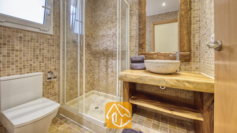 Holiday villas Costa Brava Spain - Villa Nicky - Bathroom with a glass-enclosed corner shower, a stone basin on a live-edge wooden vanity, and beige mosaic tile walls.