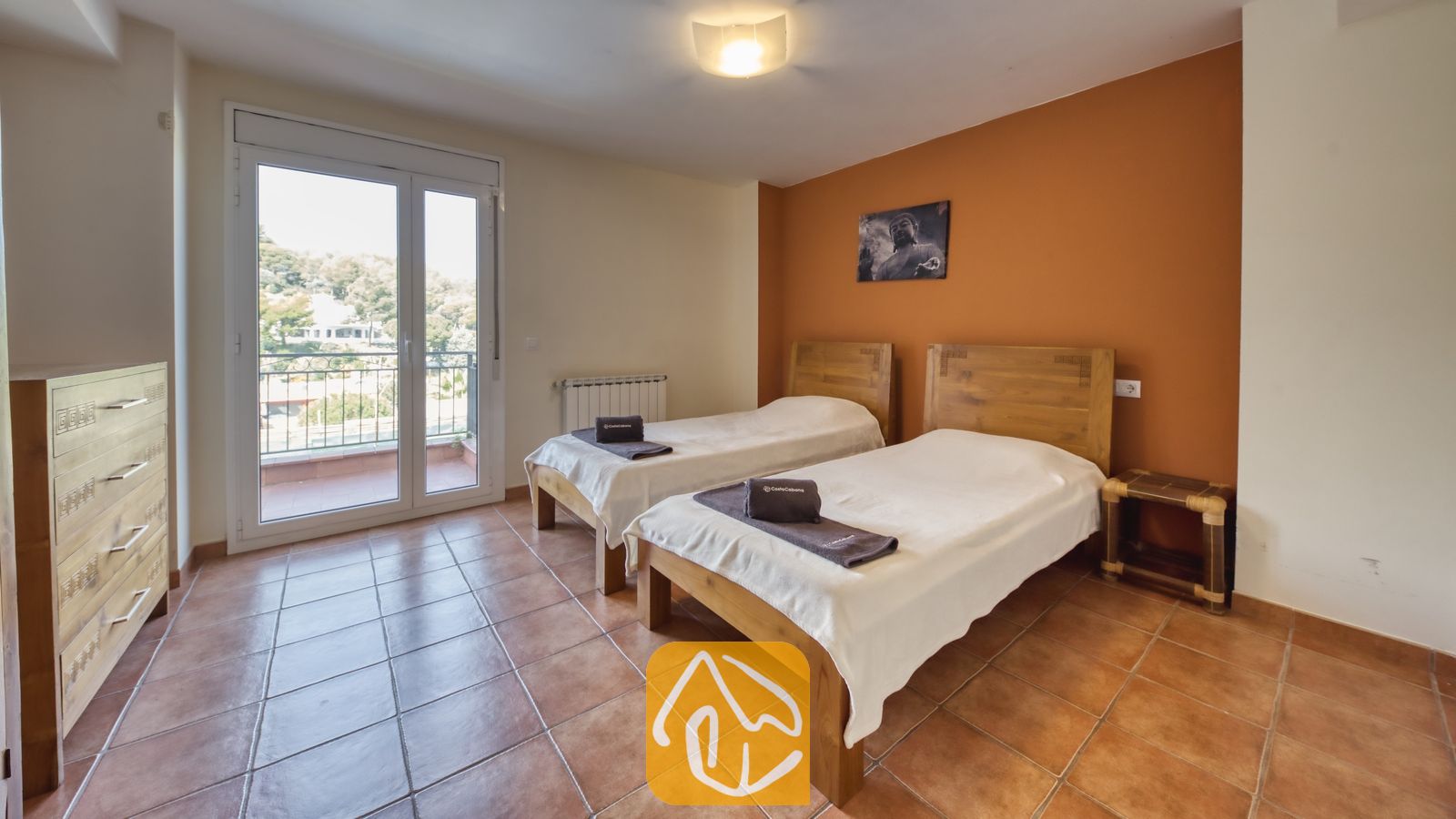 Vakantievilla's Costa Brava Spanje - Villa Nicky - Slaapkamer met twee eenpersoonsbedden, houten hoofdborden, opgerolde donkere handdoeken op witte spreien, tegelvloeren en een balkondeur met uitzicht op bomen.
