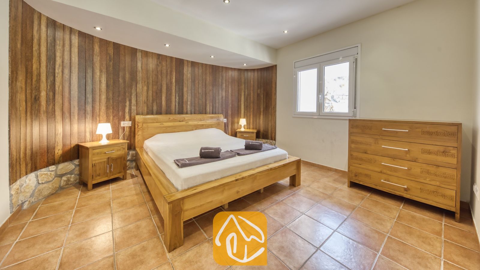 Vakantievilla's Costa Brava Spanje - Villa Nicky - Slaapkamer met een houten tweepersoonsbed, bijpassende nachtkastjes met schemerlampen en een verticale houten accentmuur achter het hoofdeinde.