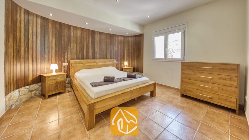 Holiday villas Costa Brava Spain - Villa Nicky - Bedroom featuring a wooden double bed, matching bedside tables with lamps, and vertical wood-paneled accent wall behind the headboard.