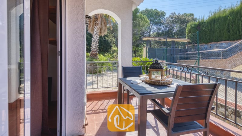 Vakantievilla's Costa Brava Spanje - Villa Nicky - Balkon van Villa Nicky met een donkerhouten eettafel, stoelen, een decoratieve lantaarn en tegelvloer met uitzicht op bomen en omheiningen.