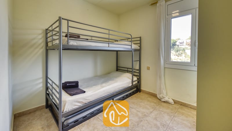 Holiday villas Costa Brava Spain - Villa Nicky - Bedroom featuring a grey metal bunk bed with white linens and folded dark towels, tiled flooring, and a small window with white curtains.