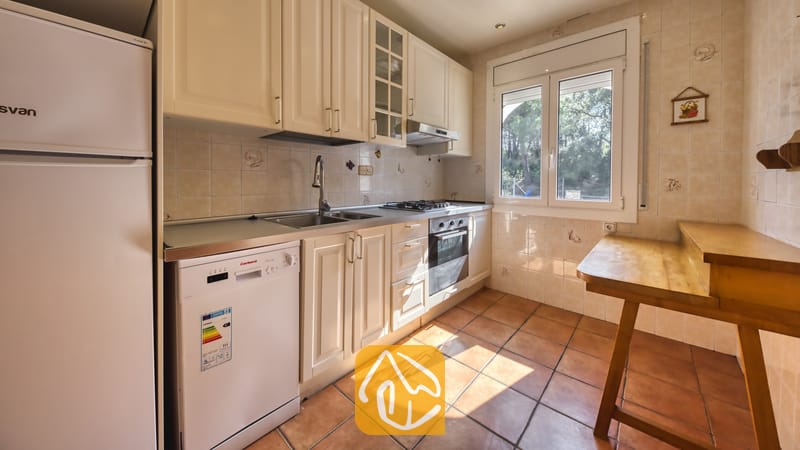 Vakantievilla's Costa Brava Spanje - Villa Nicky - Keuken met witte kasten, inbouwoven, vaatwasser, betegelde muren en een houten bartafel bij het raam.