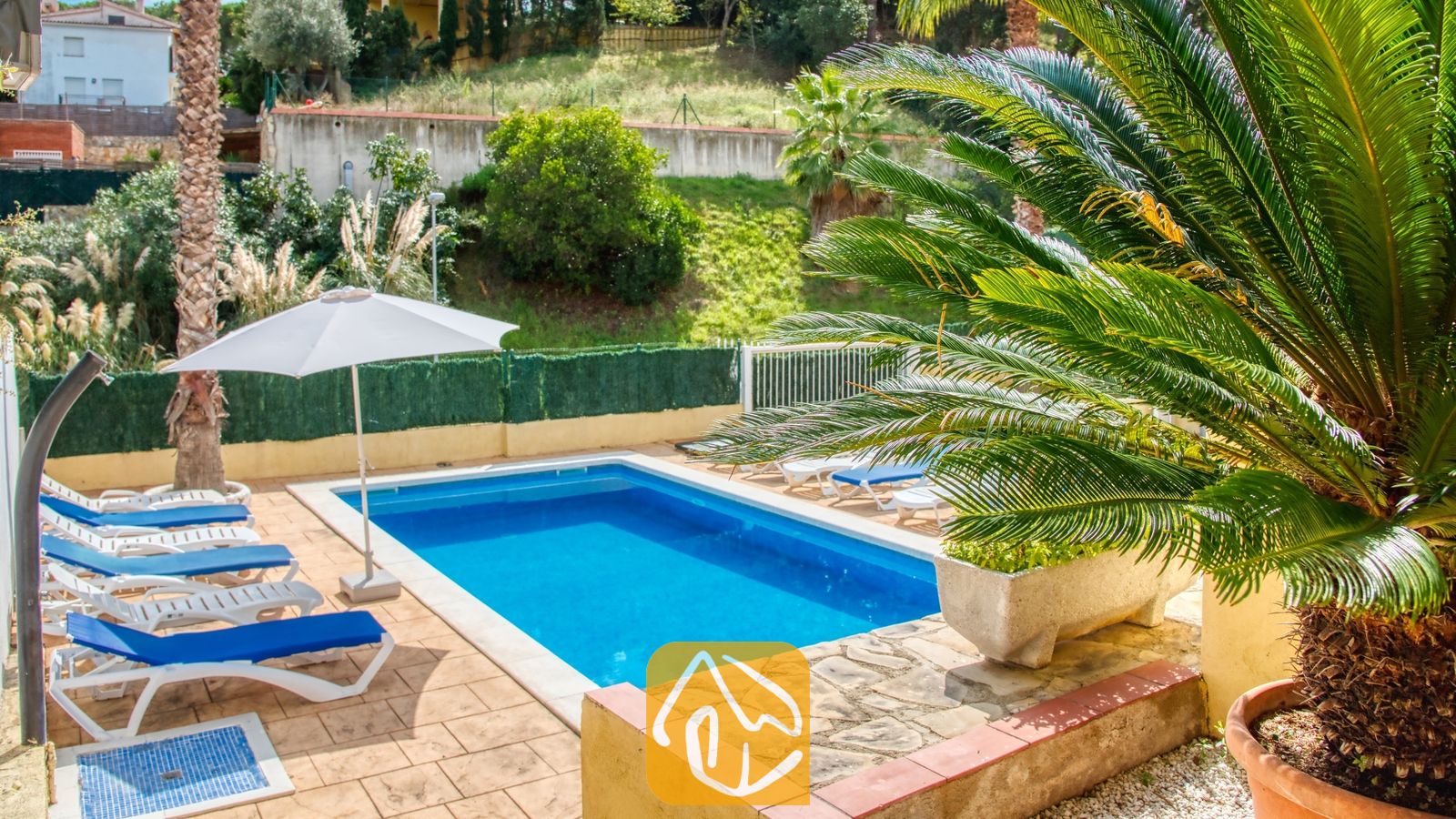 Vakantievilla's Costa Brava Spanje - Villa Ashley - Privézwembad bij Villa Ashley met helderblauw water, wit-blauwe ligbedden, een witte parasol en palmbomen op een betegeld terras.