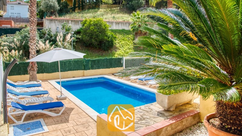 Vakantievilla's Costa Brava Spanje - Villa Ashley - Privézwembad bij Villa Ashley met helderblauw water, wit-blauwe ligbedden, een witte parasol en palmbomen op een betegeld terras.