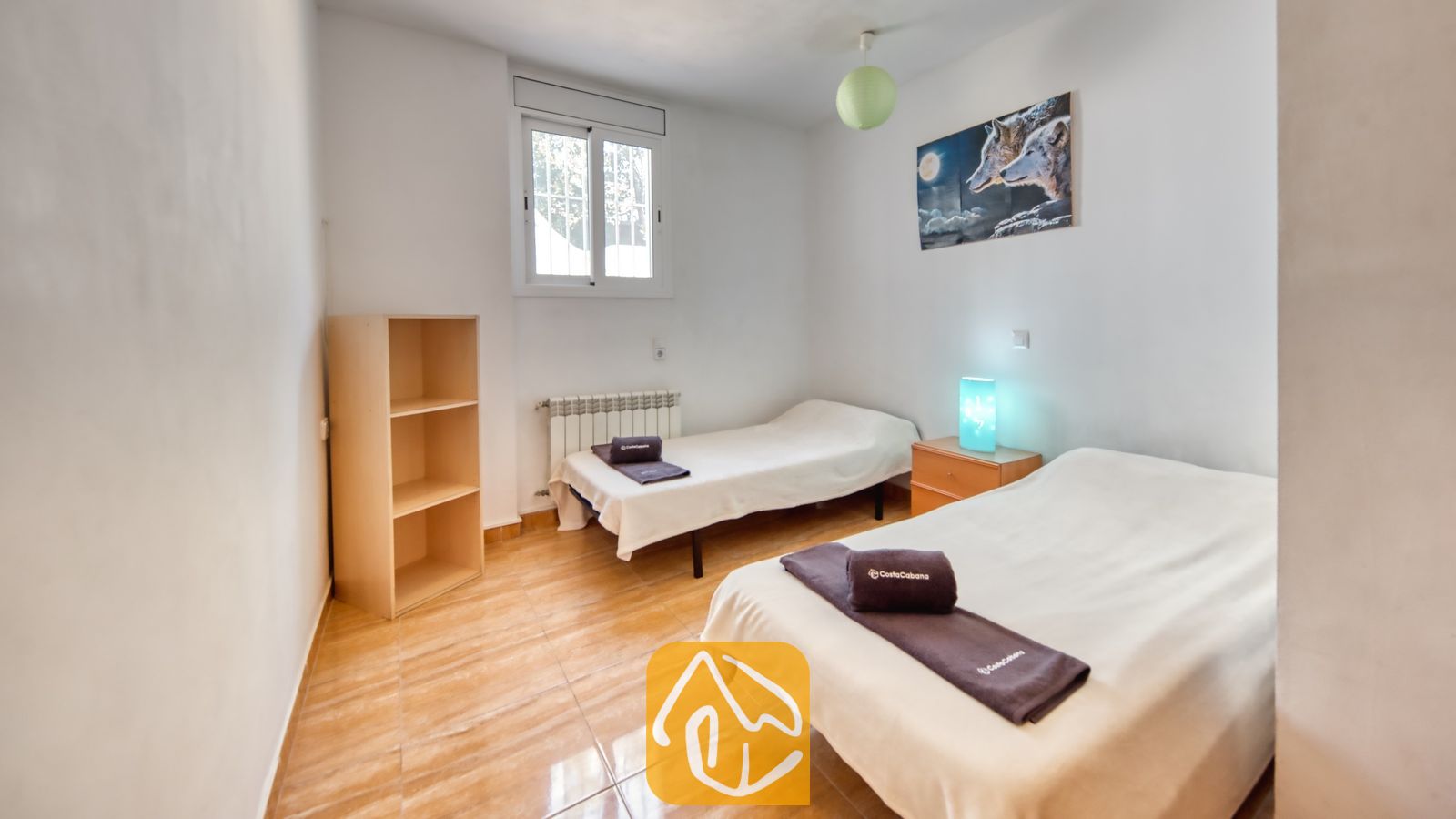 Vakantievilla's Costa Brava Spanje - Villa Ashley - Slaapkamer in Villa Ashley, voorzien van twee eenpersoonsbedden met wit beddengoed, een tegelvloer en een blauwe bedlamp. Aan de witte muur hangt een kunstwerk van een wolf.