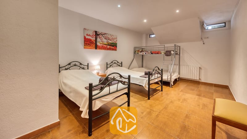 Villas de vacances Costa Brava Espagne - Villa Ashley - Chambre équipée de deux lits simples en métal noir et d'un lit superposé à la Villa Ashley. La pièce dispose d'un sol carrelé chaleureux, de murs blancs et d'une peinture paysagère colorée.