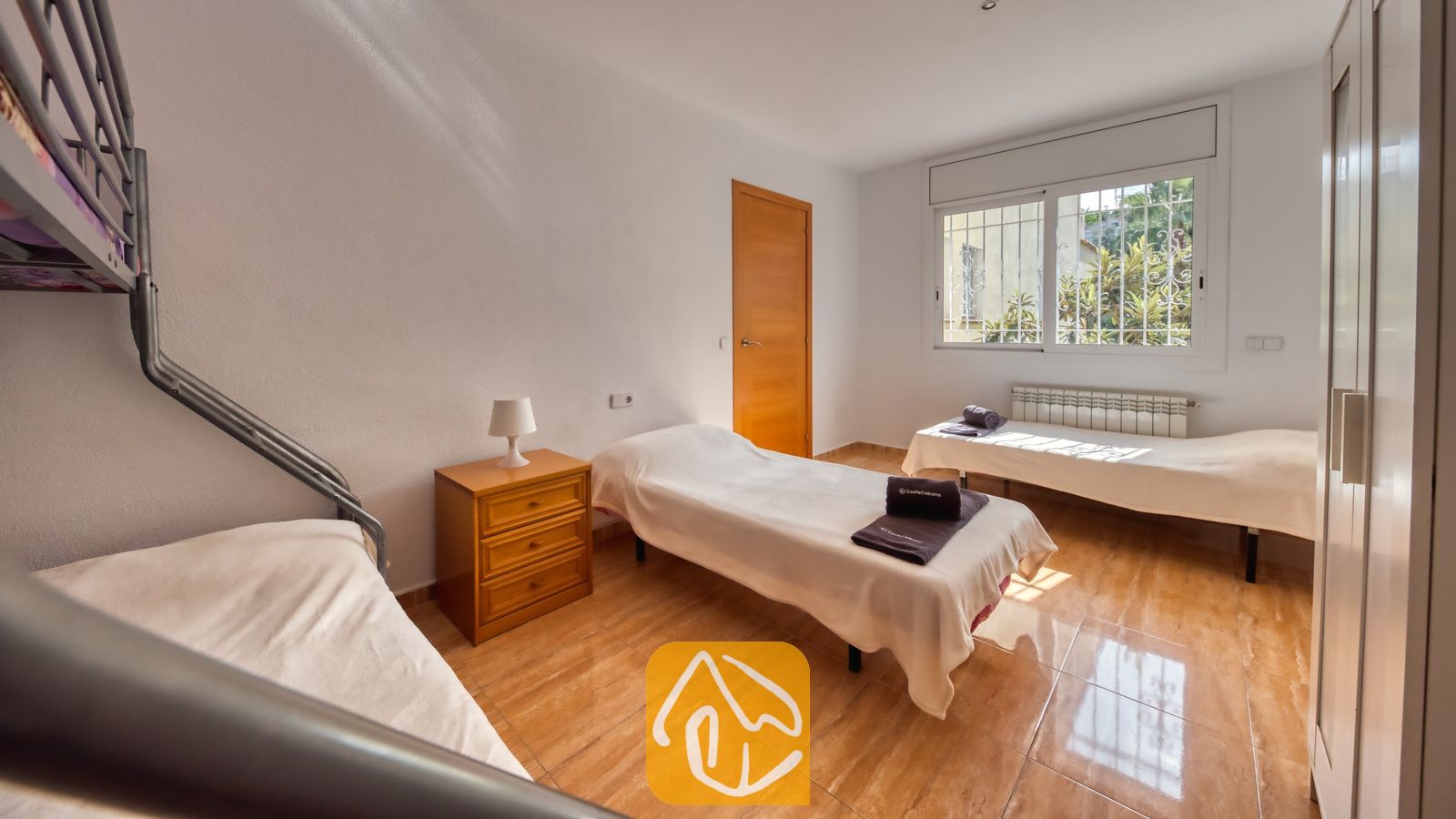 Vakantievilla's Costa Brava Spanje - Villa Ashley - Slaapkamer in Villa Ashley, voorzien van twee eenpersoonsbedden met wit beddengoed, een houten nachtkastje en een raam met traliewerk, gelegen op een tegelvloer.