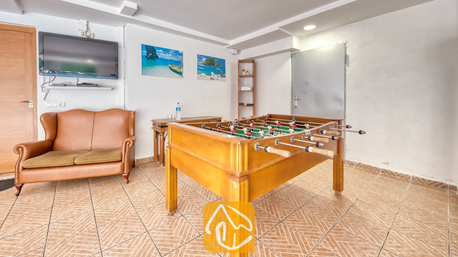 Vakantievilla's Costa Brava Spanje - Villa Ashley - In de recreatieruimte van Villa Ashley staat een houten tafelvoetbalspel op een tegelvloer, aangevuld met een leren bank en een televisie aan de muur.