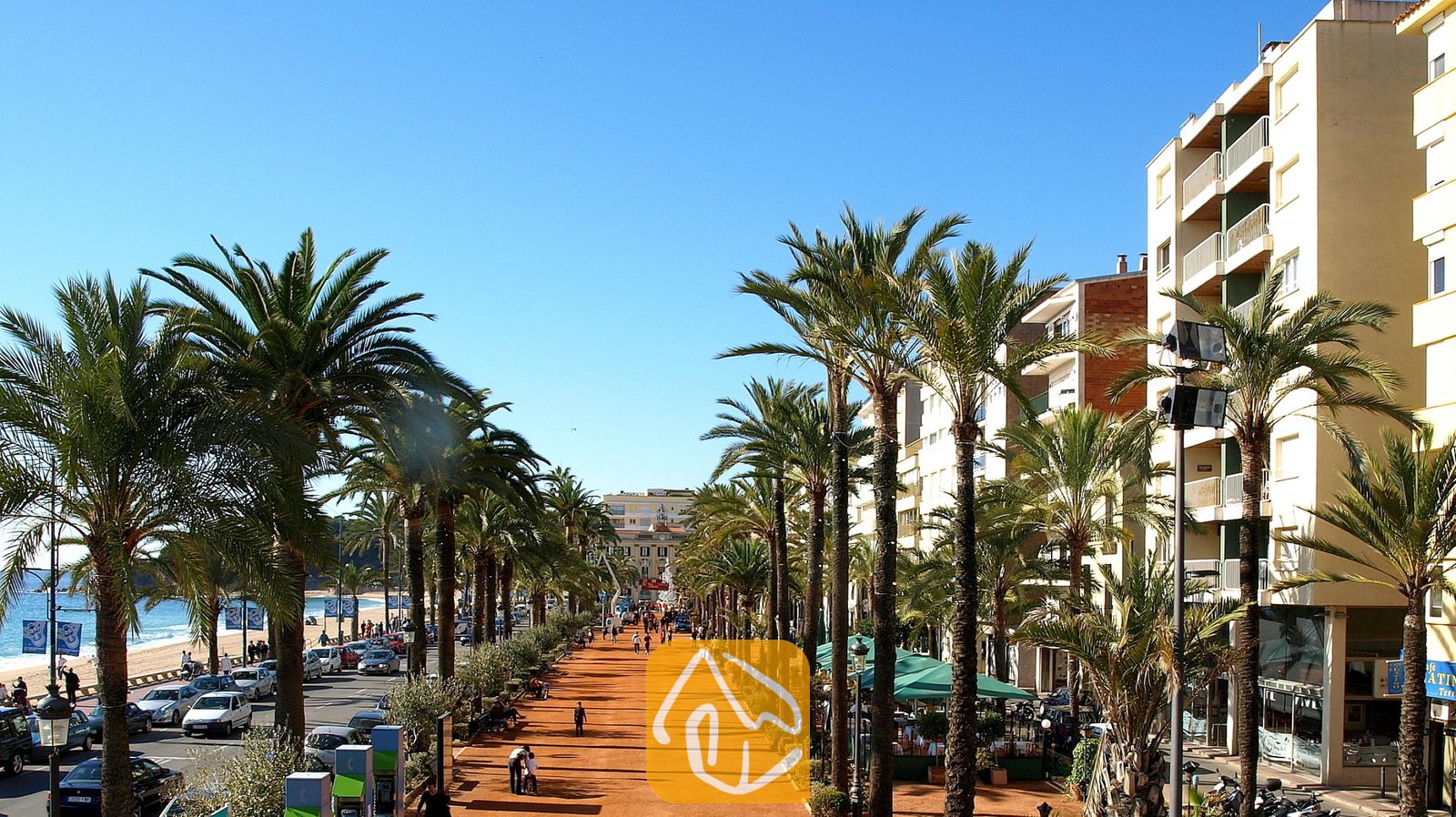 Vakantievilla's Costa Brava Spanje - Villa Pilar - Zonnige wandelpromenade met hoge palmbomen en appartementencomplexen langs een kustweg in Spanje.