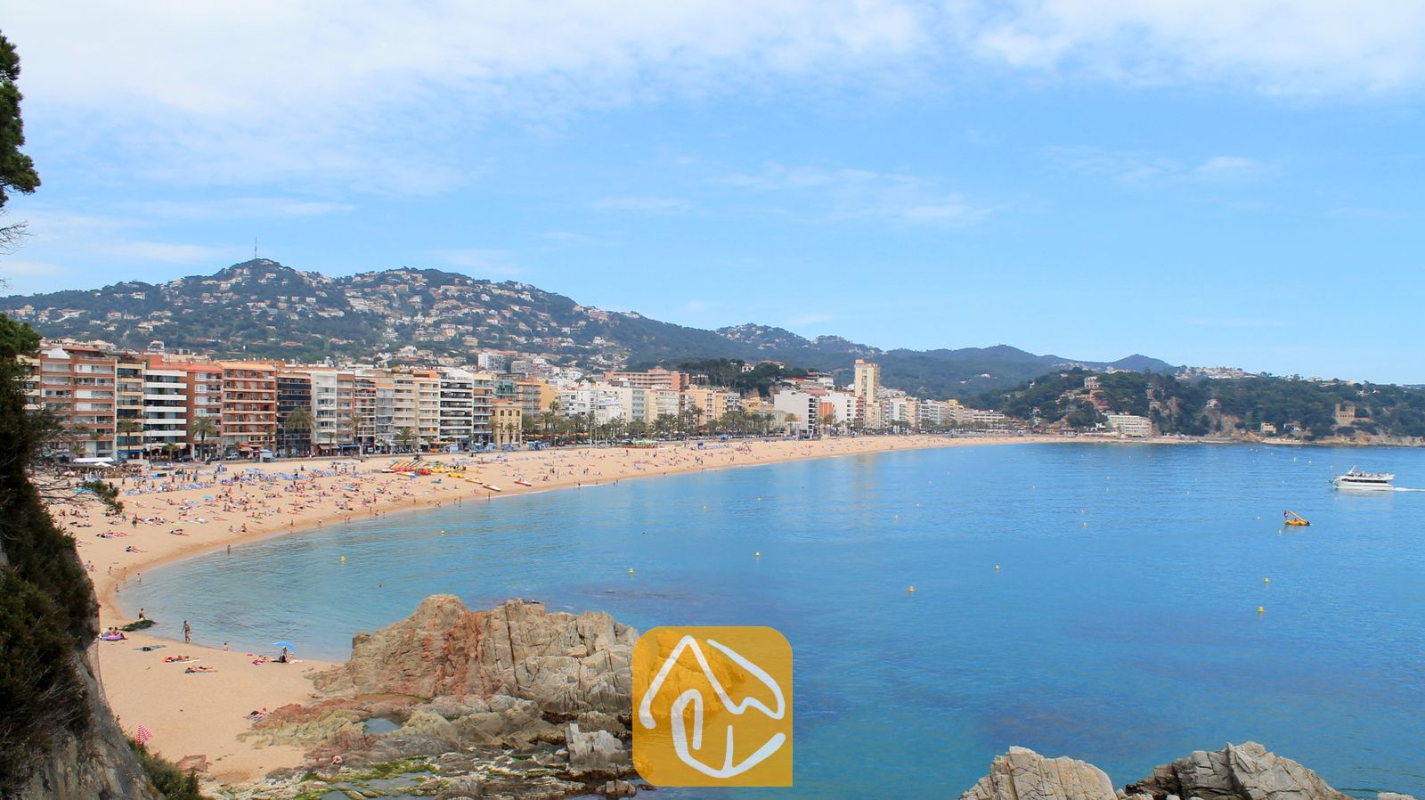 Vakantievilla's Costa Brava Spanje - Villa Pilar - Kustuitzicht vanaf Villa Pilar met een breed zandstrand, blauw water, rij aan appartementencomplexen en verre groene heuvels onder een blauwe hemel.