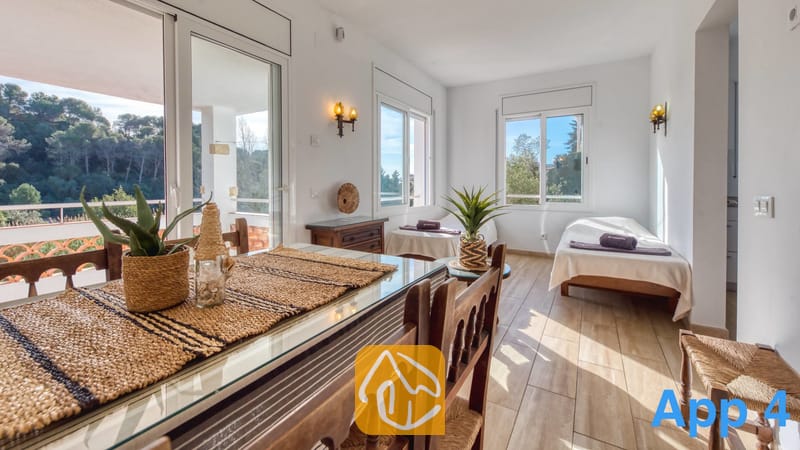 Villas de vacances Costa Brava Espagne - Villa Pilar - Espace salle à manger et nuit lumineux au sein de la Villa Pilar, comprenant une table en bois avec plateau en verre et set de table tressé, un sol en carrelage et de grandes fenêtres offrant une vue sur l'extérieur.