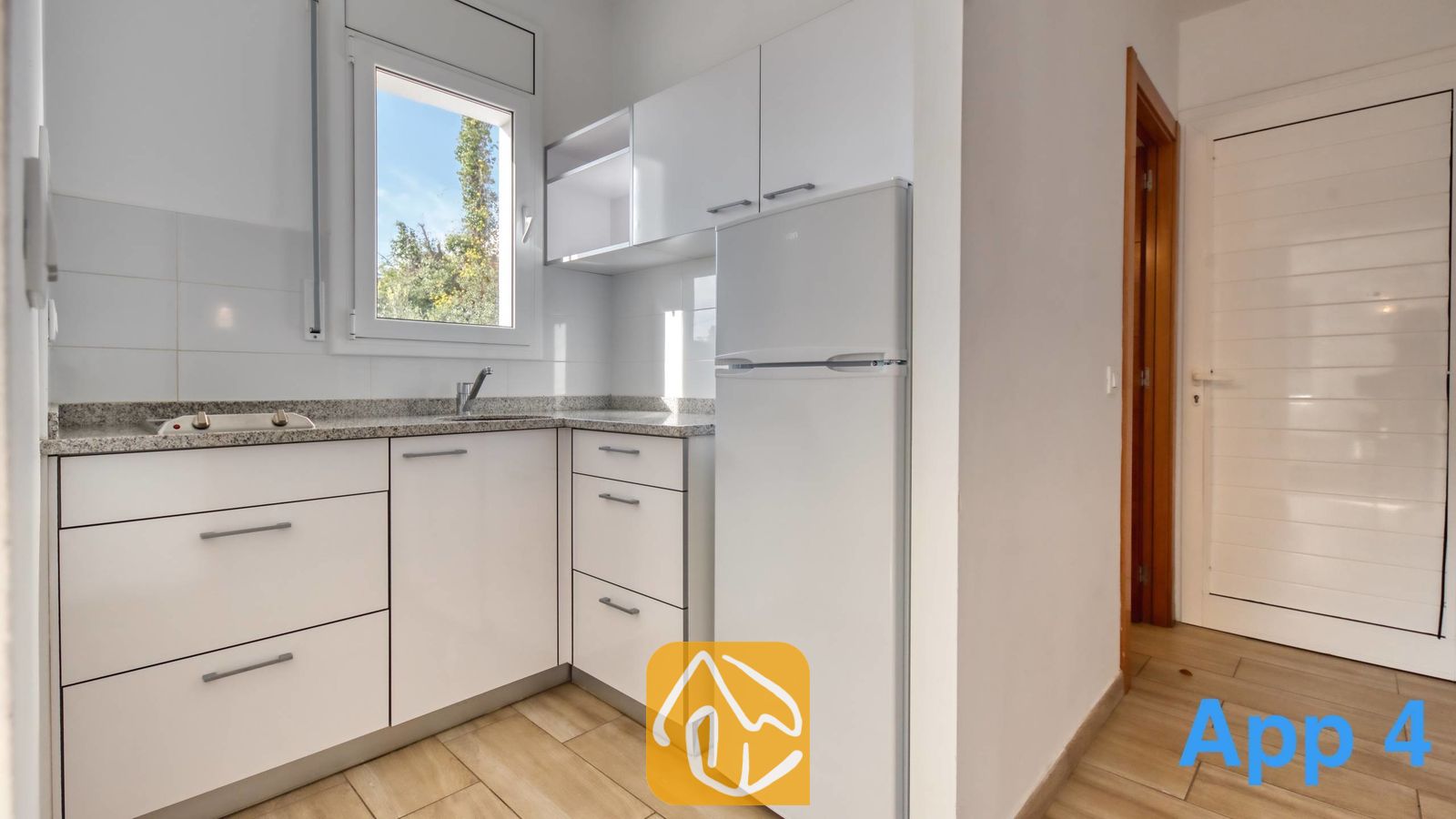 Vakantievilla's Costa Brava Spanje - Villa Pilar - Compacte kookhoek met witte kasten, granieten aanrechtbladen met spikkelpatroon, een kleine koelkast en een raam dat uitzicht biedt op het groen buiten.